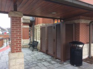 Brown metal, horizontal louvered screening enclosure under commercial awning.