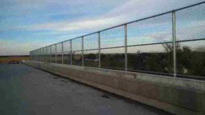 Tall, custom chain link railing atop cement wall. Kearney fence company commercial fencing contractors Kearney, Nebraska commercial industrial high security correctional recreational sport ballfield tennis court basketball pickleball football stadium track high school college playground manufacturing prison cell tower chain link barbwire gate posts tubing pipe top rail chain link fabric wire mesh galvanized aluminum vinyl coated black brown green 9 gauge fence fencing security perimeter razor concertina wire hinges installation repair costs panels hardware fittings 